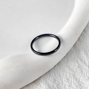 Close-up of minimalist black stainless steel ring on a white textured background
