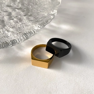 Detail of square signet rings in polished gold and sleek black finishes on white surface