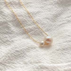 Gros plan d'un pendentif double perles d'eau douce avec chaîne dorée sur tissu blanc
