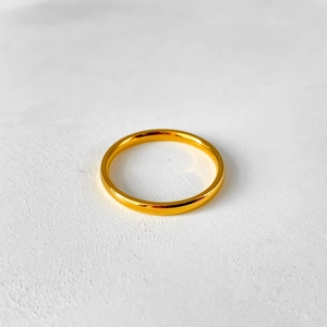 Top view of a minimalist gold polished stainless steel ring on a white textured surface