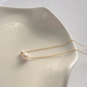 Détail d'un collier chaîne dorée minimaliste avec deux perles d'eau douce rondes