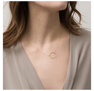Detail of a minimalist gold necklace with a hammered round pendant on a model neckline