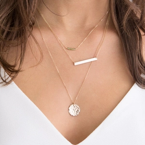 Close-up of a triple-layered gold necklace with green beads, a bar, and a hammered disc pendant