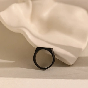 Minimalist matte black square signet ring for men on a textured cream decorative surface