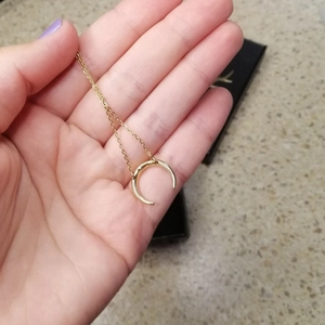 Macro detail of a minimalist gold crescent moon pendant on a delicate snake bone chain
