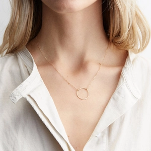 Detail of minimalist gold hammer-textured circular pendant on a fine O-chain necklace