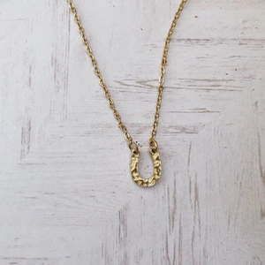 Macro shot of horseshoe pendant with hammered gold texture on a delicate chain