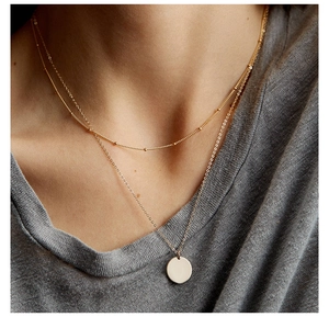 Dettaglio di collana a strati dorata con catena a sfere e ciondolo rotondo