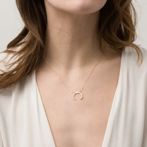 Close-up of a delicate gold crescent moon necklace on a woman with a modern V-neck dress