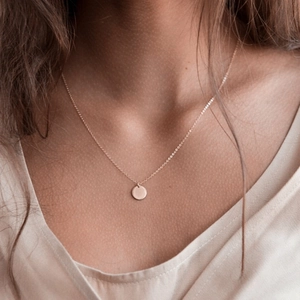 Close-up of a minimalist rose gold round pendant necklace worn on a woman's collarbone