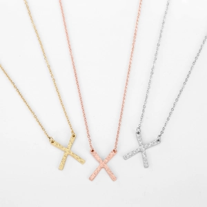 Detailed view of three X-shaped necklaces with hammered texture in gold, rose gold and silver