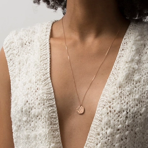 Close-up of hammered rose gold coin necklace on neck with textured finish