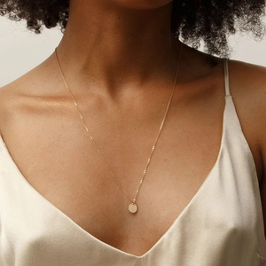 Minimalist gold necklace with round pendant shown on a model wearing a silk dress