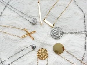 Minimalist gold and silver necklaces with geometric pendants on a white lace background