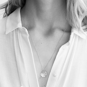 Detailed view of a silver-tone hammered coin pendant on a delicate chain necklace