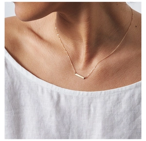 Close-up of a minimalist gold horizontal bar pendant necklace worn by a female model