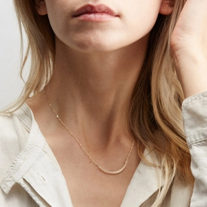 Dettaglio della collana minimalista con barra curva dorata indossata su camicia