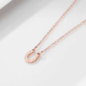 Close-up of horseshoe pendant with rose gold hammered texture and thin chain