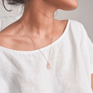 Detail of rose gold oval pendant necklace with hammered finish on female model