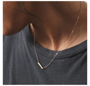 Close-up of a minimalist golden bar pendant necklace on a model's collarbone