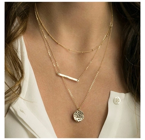 Detailed view of triple-layered gold necklaces with coin and hammered bar pendants