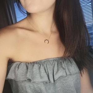 Detailed view of a gold moon crescent pendant necklace worn on a model with a grey top