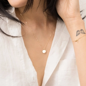 Minimalist gold geometric circular pendant necklace and bracelet set on model with linen