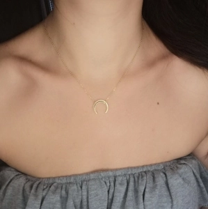 Detail of a polished gold-plated crescent moon pendant on a fine snake chain necklace