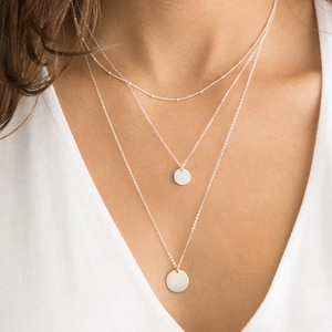 Three-layer silver bead chain necklace with round pendants on a white shirt