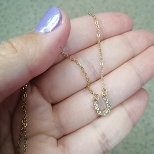 Gold hammered U-shape horseshoe pendant necklace held in hand on a textured surface
