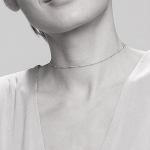 Detailed view of delicate silver bead chain necklace worn on a woman's collarbone