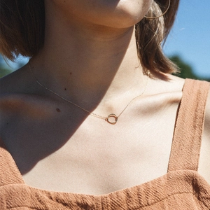Minimalist gold circle pendant necklace for women worn by model against a blue sky