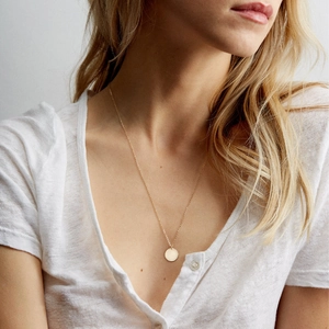 Collier minimaliste avec pendentif rond plaqué or porté par un mannequin en lin blanc