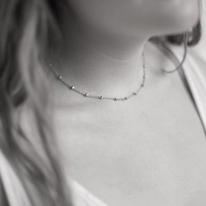 Close-up of minimalist stainless steel bead chain necklace worn on a woman's neck