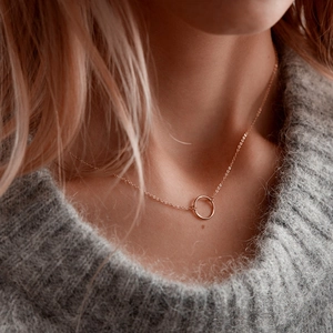 Close-up of minimalist rose gold geometric circular necklace worn on a grey knit sweater