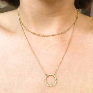Close-up of gold double-layered necklace with round beads and hammered pendant on model