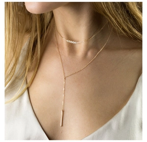 Close-up of layered gold titanium necklace set with white pearls and long bar pendant