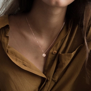 Close-up of a rose gold minimalist round pendant necklace on a female model
