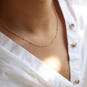 Close-up of a delicate gold satellite bead chain necklace worn on the collarbone