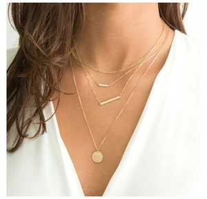 Detailed view of layered gold necklace set with pearl, bar, and hammered disc charms