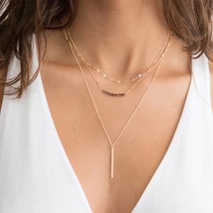 Detailed view of triple-layered gold necklace with red beads and vertical bar pendant