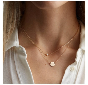 Détail d'un collier doré multicouche avec perle d'eau douce et pendentif rond poli