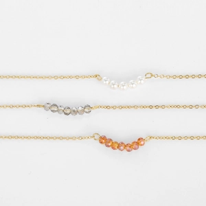 Trois colliers en acier doré avec des perles de cristal blanches, grises et oranges