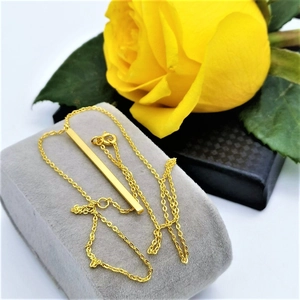 Detail of a minimalist gold vertical bar pendant necklace on a jewelry display