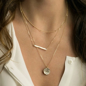 Three-layer gold necklace featuring beaded chain and hammered bar and disc pendants
