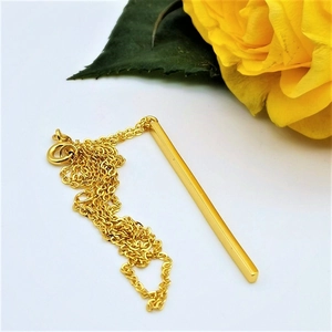 Polished gold rectangular bar pendant necklace on white background with a yellow rose