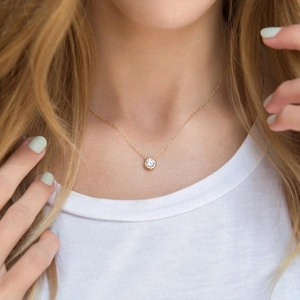 Close-up of a minimalist gold zircon pendant necklace worn by a model on a white top