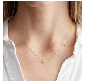 Élégant collier doré avec pendentif perle d'eau douce porté par un mannequin en chemise blanche