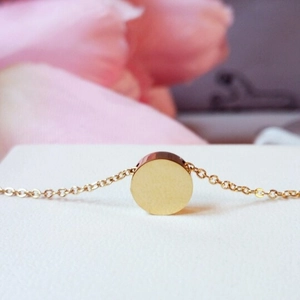 Minimalist gold stainless steel necklace with round pendant on white display with flowers