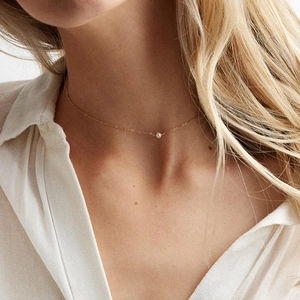 Detail of a minimalist gold necklace with a single white pearl pendant on a delicate chain